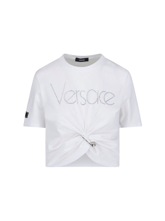 Versace T-Shirt Crop "1978 Re-Edition"-t-shirt-Versace-T-shirt crop "1978 re-edition" Versace, in cotone bianco, girocollo, maniche corte, etichetta logo applicata manica, dettaglio logo cristalli frontale, dettaglio spilla frontale, orlo annodato.-Dresso