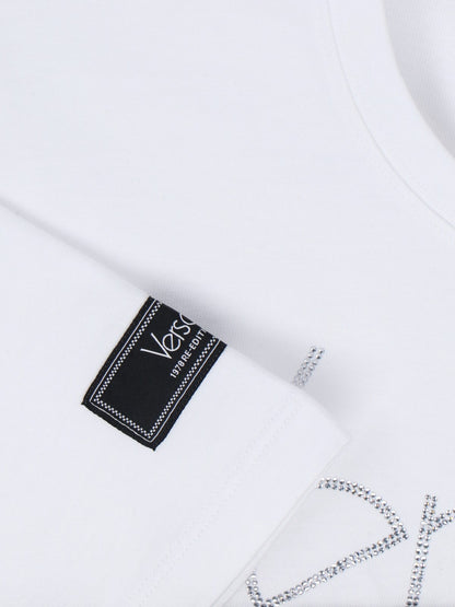Versace T-Shirt Crop "1978 Re-Edition"-t-shirt-Versace-T-shirt crop "1978 re-edition" Versace, in cotone bianco, girocollo, maniche corte, etichetta logo applicata manica, dettaglio logo cristalli frontale, dettaglio spilla frontale, orlo annodato.-Dresso